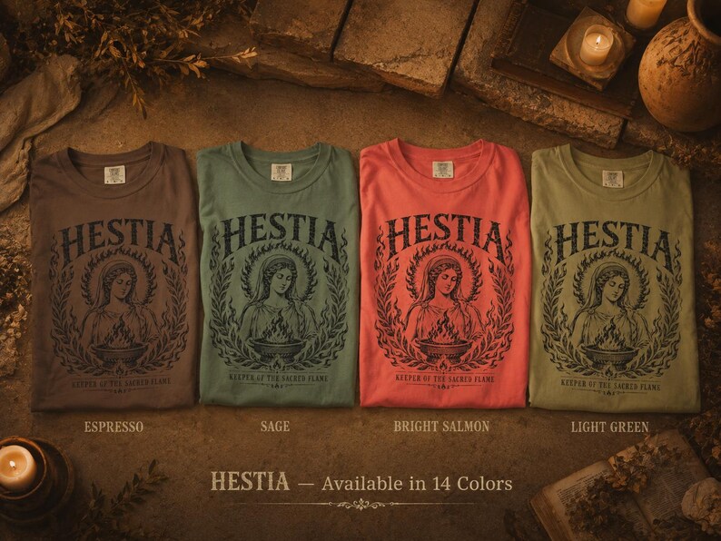 May include: Four crew neck t-shirts in espresso, sage, bright salmon, and light green. Each shirt features the word "HESTIA" above a graphic of a woman with a flame and the text "KEEPER OF THE SACRED FLAME". The text "HESTIA - Available in 14 Colors" is at the bottom.