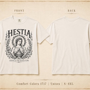 May include: A white t-shirt featuring a graphic of Hestia, the Greek goddess of the hearth, with the text "HESTIA" above her and "KEEPER OF THE SACRED FLAME" below. The back of the shirt is plain white. The shirt is labeled as Comfort Colors 1717, Unisex, and available in sizes S-4XL.