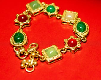 May include: A gold-tone link bracelet featuring alternating square and star-shaped settings. The bracelet is adorned with smooth, cabochon-style stones in shades of deep green, light green, red, and cream, connected by a lobster claw clasp.