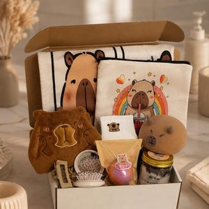 May include: A gift box containing a capybara-themed canvas pouch with a rainbow graphic, a brown plush bear-shaped item, a pair of white socks with a small bear icon, a round bath bomb, a small jar of bath salts, a hair clip, and a small hairbrush.