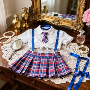 Op de afbeelding: Een wit kort shirt met korte mouwen, kraag en strikdetail aan de voorzijde, gecombineerd met een rood, blauw en wit geruite plooirok. De set bevat blauwe bretels, een bijpassende geruite stropdas en een blauwe choker met zilverkleurige gesp.