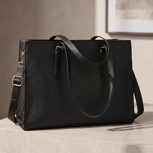 May include: A structured black rectangular tote bag with a smooth finish, featuring two top handles with gold-tone buckles and a detachable, adjustable shoulder strap with a gold-tone metal slider and clasp hardware on the side.