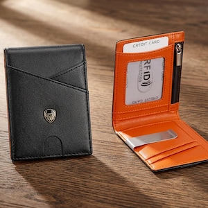 May include: A black leather wallet with a gold-toned emblem on the front and a bright orange interior. The wallet features a clear ID window, a zippered pocket, multiple card slots, and a silver-toned metal money clip for holding currency.