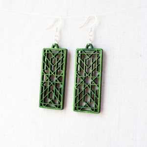 May include: A pair of green wooden earrings with a geometric design. The earrings are rectangular in shape and have a delicate, intricate pattern.
