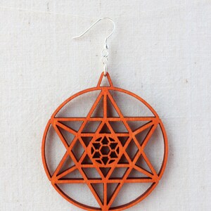 May include: A pair of wooden earrings with a geometric design. The earrings are a reddish-brown colour and feature a circular shape with a star-shaped pattern inside.