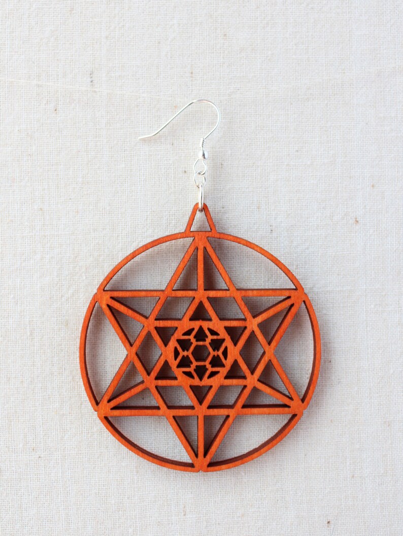 May include: A pair of wooden earrings with a geometric design. The earrings are a reddish-brown colour and feature a circular shape with a star-shaped pattern inside.