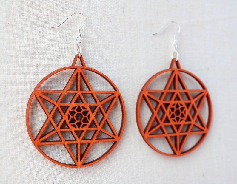 May include: A pair of orange wooden earrings with a geometric star design. The earrings are made of wood and have a silver hook.