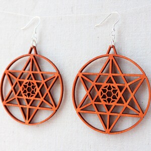 May include: A pair of wooden earrings featuring a geometric star design. The earrings are a reddish-brown colour and have silver hooks.
