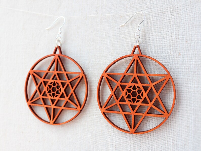 May include: A pair of wooden earrings featuring a geometric star design. The earrings are a reddish-brown colour and have silver hooks.