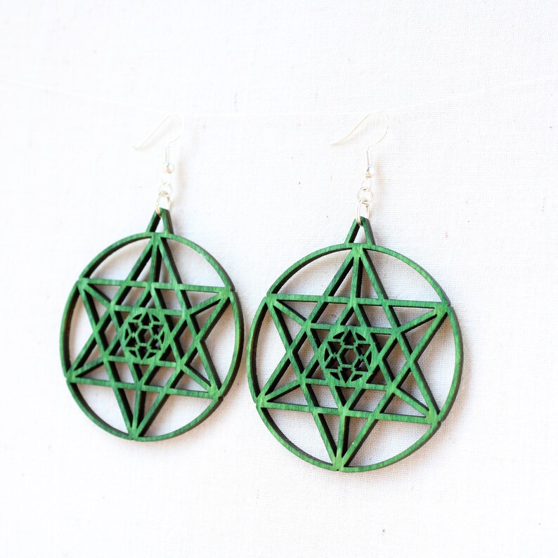 May include: A pair of green wooden earrings with a geometric star design. The earrings are made of wood and have a silver hook.