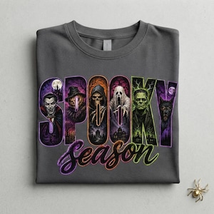 Puede incluir: Una camiseta gris carbón con el texto SPOOKY SEASON en letras grandes. Cada letra contiene ilustraciones detalladas de personajes de terror, incluyendo un vampiro, una calabaza, la muerte, un fantasma, Frankenstein y un hombre lobo.