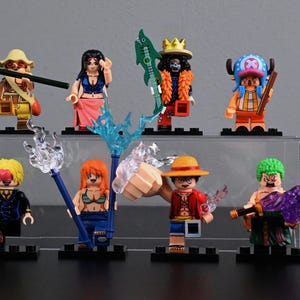 Könnte beinhalten: Eine Sammlung von acht farbenfrohen Minifiguren, jede mit einzigartigen Outfits und Accessoires. Die Figuren sind auf einem transparenten Displayständer mit grauem Hintergrund angeordnet. Die Figuren scheinen von einer beliebten Anime-Serie inspiriert zu sein.