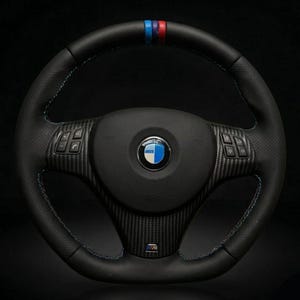 Könnte beinhalten: Ein schwarzes Lederlenkrad mit einer Mittelblende aus Carbon, blauen und roten Ziernähten sowie einem dreifarbigen Streifen oben. In der Mitte befindet sich ein rundes BMW-Logo und integrierte Bedientasten an den linken und rechten Speichen.