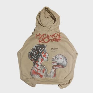 以下が含まれることがあります： 上部に赤い文字でMy Chemical Romanceと書かれたベージュのフード付きスウェットシャツ。その下には、暗い髪で顔や服に赤い模様がある人物が頭蓋骨を持っているグラフィックが描かれています。小さな文字で、Cause the hardest part of this is leaving you.と書かれています。