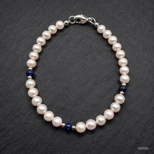 May include: A bracelet featuring a continuous strand of white pearls interspersed with three small, round, dark blue beads and silver-toned metal spacers. The piece is secured with a silver-toned lobster claw clasp at the top of the circular arrangement.