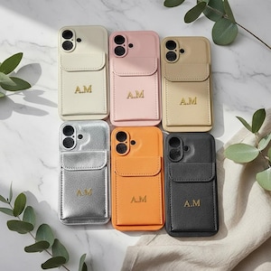 Puede incluir: Seis fundas rectangulares para teléfono en blanco, rosa, beige, plateado, naranja y negro, cada una con acabado texturizado, bolsillo con solapa y las iniciales A.M. grabadas en oro en el centro. Cada funda tiene un recorte para doble cámara.