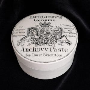 May include: A round white ceramic pot for Burgess's Genuine Anchovy Paste. The lid features black printed text and a royal crest illustration with a lion and unicorn, including the address 107 Strand corner of the Savoy steps London.