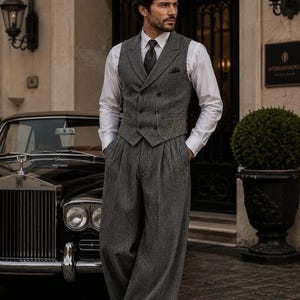 May include: A grey herringbone patterned double-breasted vest and matching wide-leg trousers paired with a crisp white long-sleeve button-down shirt, a dark tie, and a pocket square. A thin gold chain is attached to the front of the vest.