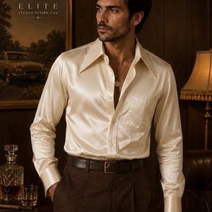 May include: A long-sleeved, cream-colored satin shirt with a wide pointed collar, a single chest pocket, and buttoned cuffs. The shirt is worn tucked into dark brown trousers secured with a simple dark brown leather belt and a metal buckle.
