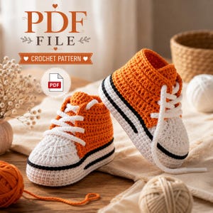 May include: A pair of orange and white crocheted baby trainers with white laces and black trim. The image includes text that reads PDF FILE CROCHET PATTERN. The design features a high-top style with a textured stitch pattern and a rounded toe.