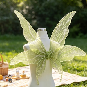 Peut inclure: Une paire d'ailes de fée translucides vert clair fixées sur un torse de mannequin blanc. Les ailes présentent un motif délicat de paillettes argentées scintillantes avec des lignes complexes semblables à des nervures sur tout le tissu.