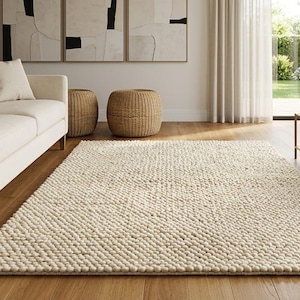 Puede incluir: Una alfombra rectangular con una textura gruesa de lana anudada a mano en un color crema sólido. La alfombra presenta un patrón de tejido denso y elevado similar a pequeñas protuberancias que cubre toda la superficie de forma uniforme.