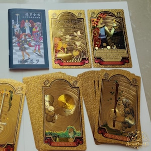 May include: A set of gold-foiled tarot cards featuring intricate embossed designs and a small instructional booklet with Chinese text. The cards display various symbolic illustrations including hands holding coins and wands, all rendered in a metallic finish.
