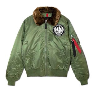 May include: An olive green bomber jacket featuring a brown faux fur collar, a central silver zipper, and ribbed cuffs and hem. A circular patch on the chest displays a skull with wings and the text TASK FORCE VANGUARD. A utility pocket with black and red ribbons is on the sleeve.