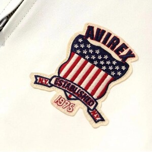 May include: Embroidered patch featuring a shield design with red and white stripes and a blue field of stars. The patch reads "AVIREX" and "ESTABLISHED 1975" with "N.Y." on the banner. The patch is on a white background.