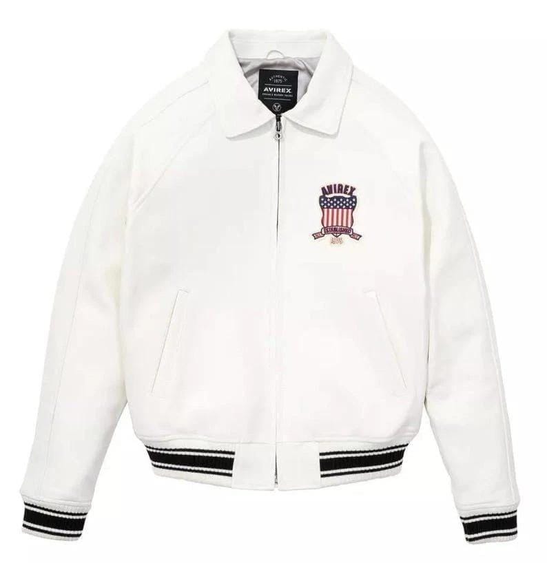 May include: A white jacket with a collared neckline and a zipper closure. The jacket features a black and white striped hem and cuffs. An embroidered emblem with the text "AVIREX" and an American flag design is on the chest.