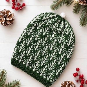 May include: A knitted beanie featuring a dark green and white zigzag pattern throughout the fabric. The hat has a ribbed hem at the base and a small, textured white pom-pom attached to the very top center of the crown, creating a winter look.