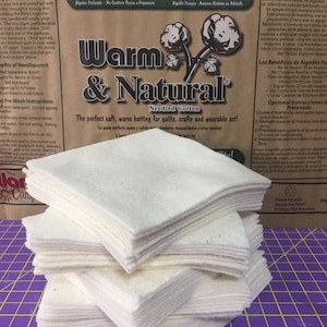 May include: A stack of 18 white, square, needle-punched cotton batting squares. The squares are made of 100% cotton and are perfect for quilting, crafts, and wearable art. The label reads "Warm & Natural Needled Cotton" and states that the batting is needle-punched, does not contain resins or glues, and is the #1 cotton in the world.