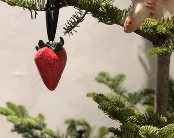 May include: A Christmas tree branch with two decorative ornaments. One is a red strawberry with green leaves, the other a star with a face. The tree has green needles.