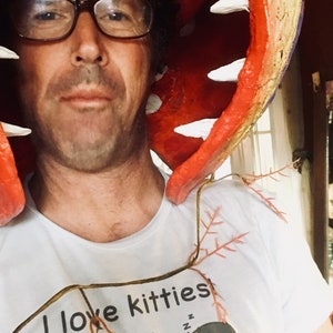 K&ouml;nnte beinhalten: Eine Person tr&auml;gt ein wei&szlig;es T-Shirt mit dem Text "I love kitties" und einem Cartoon-Katzenmotiv. Die Person tr&auml;gt ein rot-gr&uuml;nes, pflanzenartiges Kost&uuml;m mit wei&szlig;en Z&auml;hnen.