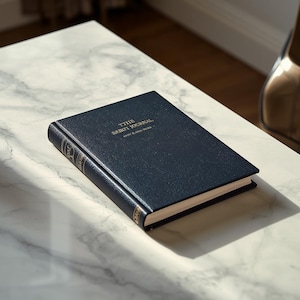 Könnte beinhalten: Ein dunkelblaues Notizbuch mit festem Einband, strukturierter Oberfläche und goldener Prägung auf dem Vorderdeckel mit der Aufschrift THE SABI JOURNAL. Der Buchrücken zeigt goldene Zierlinien und Text, cremefarbene Seiten sind sichtbar.
