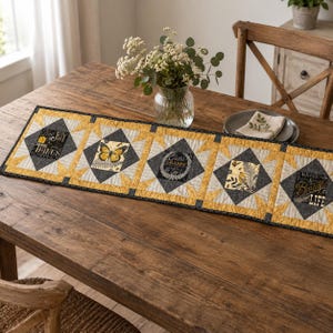 May include: A rectangular quilted table runner featuring five square panels with yellow and charcoal gray star patterns. The panels display printed graphics of a butterfly, a bird, and text reading Find Joy in the Things, Choose Happy, and Great Beautiful Life.