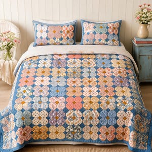 Puede incluir: Una colcha y dos fundas de almohada rectangulares a juego con un patrón floral repetitivo de parches de tela azul, rosa, amarilla y blanca. El diseño consiste en formas redondeadas interconectadas con un borde azul y una base blanca.