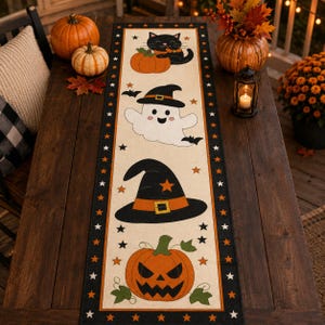 May include: A rectangular table runner with a cream-coloured centre featuring a black cat with a pumpkin, a smiling ghost wearing a witch hat, a large black witch hat, and a jack-o'-lantern. The border is black with orange stars.