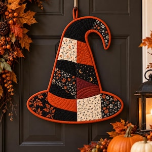 Könnte beinhalten: Ein gesteppter Wandbehang aus Stoff in Form eines Hexenhutes mit einem Patchwork-Design aus schwarzen, orangefarbenen und cremefarbenen Stoffen mit Blumen-, Blatt- und Mondsichelmustern, eingefasst mit einer leuchtend orangefarbenen Borte und Schlaufe.