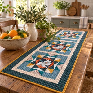Könnte beinhalten: Ein rechteckiger, gesteppter Tischläufer mit einem wiederkehrenden Sternmuster in Blaugrün, Orange, Gelb und Creme, wobei jeder Block ein zentrales Blumenmotiv aufweist. Der Läufer hat einen dunkelblaugrünen Rand mit Rautensteppung und eine gelbe Kante.