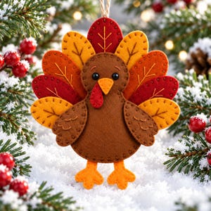 May include: A felt turkey ornament featuring a brown body, orange feet, and a fan of layered leaves in shades of red, orange, and yellow. The turkey has black bead eyes, an orange beak, and a red wattle, with a twine loop for hanging.
