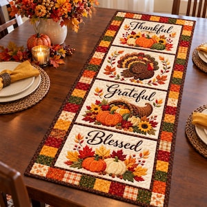 May include: A rectangular quilted table runner featuring four vertical panels with autumn-themed illustrations. The panels display pumpkins, a turkey, a cornucopia, and fall leaves, with the words Thankful, Grateful, and Blessed printed in black.