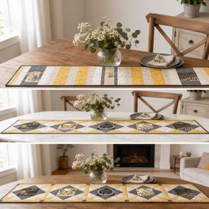 May include: A quilted table runner featuring a patchwork design of yellow and gray fabric panels. The runner displays printed graphics of butterflies, birds, and text including "Joy" and "Life" arranged in a repeating geometric pattern.