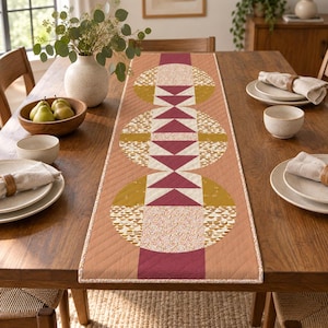 Peut inclure: Un chemin de table matelassé rectangulaire présentant un motif géométrique de cercles et de triangles dans des tons terre cuite, jaune moutarde et crème. Le design comprend des motifs circulaires répétitifs avec des textures et des blocs unis.