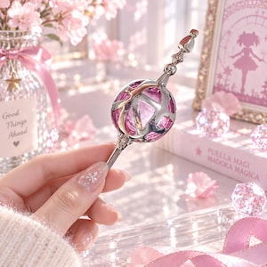 May include: A silver-toned metal scepter featuring a spherical center with a translucent pink core encased in an intricate, openwork silver frame. The handle is slender and straight, topped with a decorative, multi-faceted silver finial.