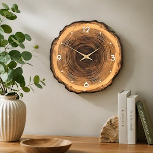 May include: A round wall clock crafted from a natural wood slice with visible dark brown tree rings. The clock face features white numerals at the 12, 3, 6, and 9 o'clock positions, with simple white dots for other hours and thin gold-coloured metal hands.