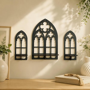 Può includere: Tre mensole da parete in legno nero con design a finestra gotica. Ogni mensola ha una parte superiore ad arco con un motivo a croce e un piccolo ripiano. Le mensole sono montate su una parete beige chiaro.