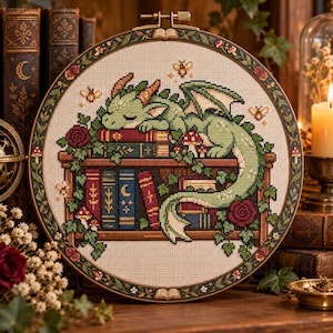 May include: A circular cross-stitch embroidery piece featuring a light green dragon sleeping on a wooden bookshelf filled with colorful books, ivy, red roses, and small mushrooms. The design is framed in a dark wooden hoop with a decorative border.