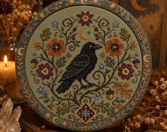May include: A circular embroidery hoop containing a cross-stitch design on sage green fabric. The design features a black crow perched on a branch, surrounded by orange and maroon flowers, small blue blossoms, acorns, and a golden crescent moon.