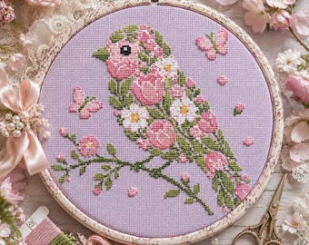 May include: A circular embroidery hoop containing a cross-stitch design of a bird composed of pink and white flowers and green leaves on a light purple fabric. The bird sits on a branch with two small butterflies and scattered petals.